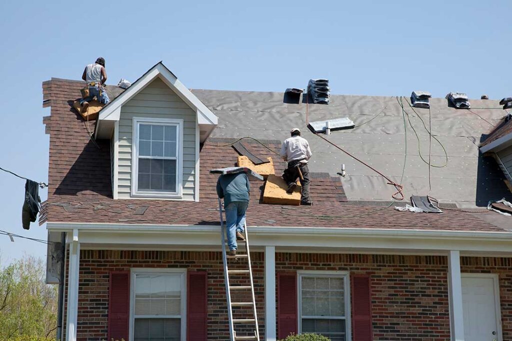 A homeowner uses a smartphone to photograph missing asphalt shingles on a house roof after a storm.