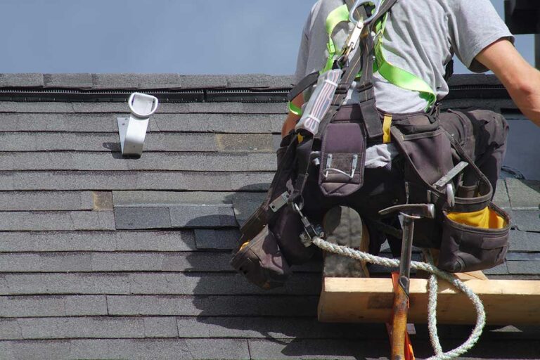 Technician inspects asphalt shingle roof while solar panels are being installed nearby.
