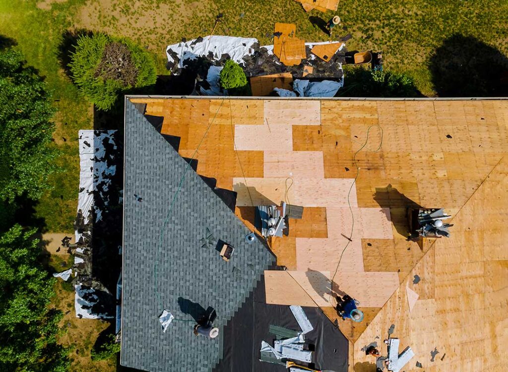 A person examining pitched residential shingles with binoculars after a rainstorm.